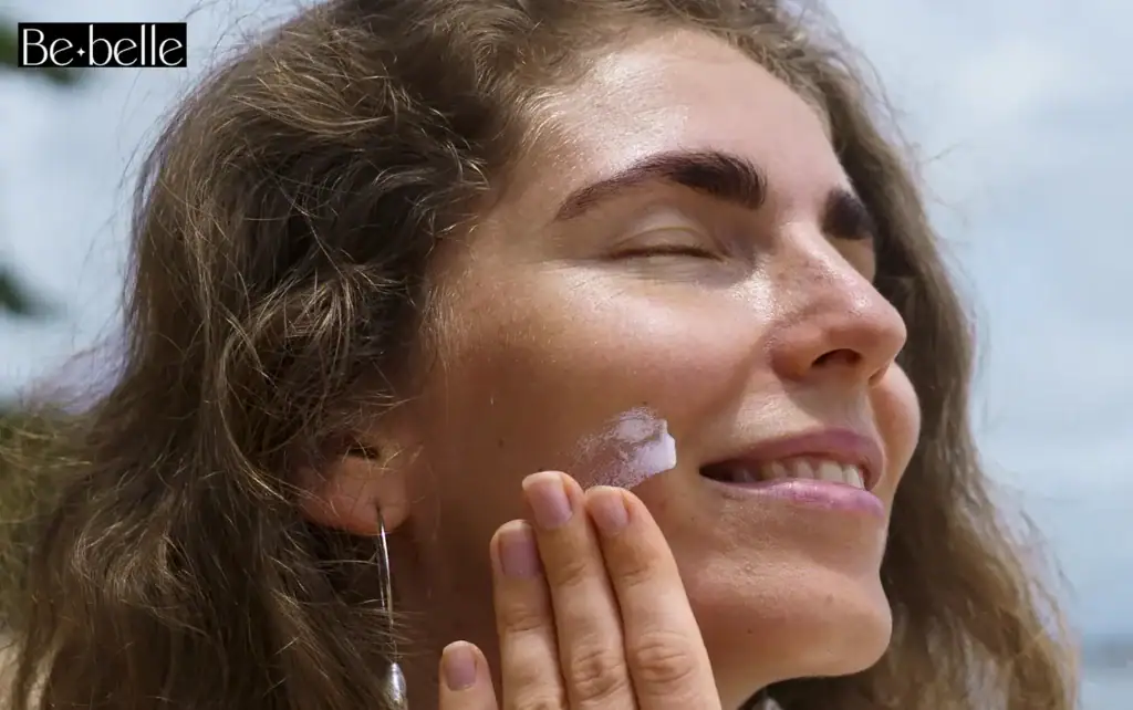 בחורה על רקע של שמיים כחולים מורחת קרם הגנה ביום שמשי עם לוגו Bebelle