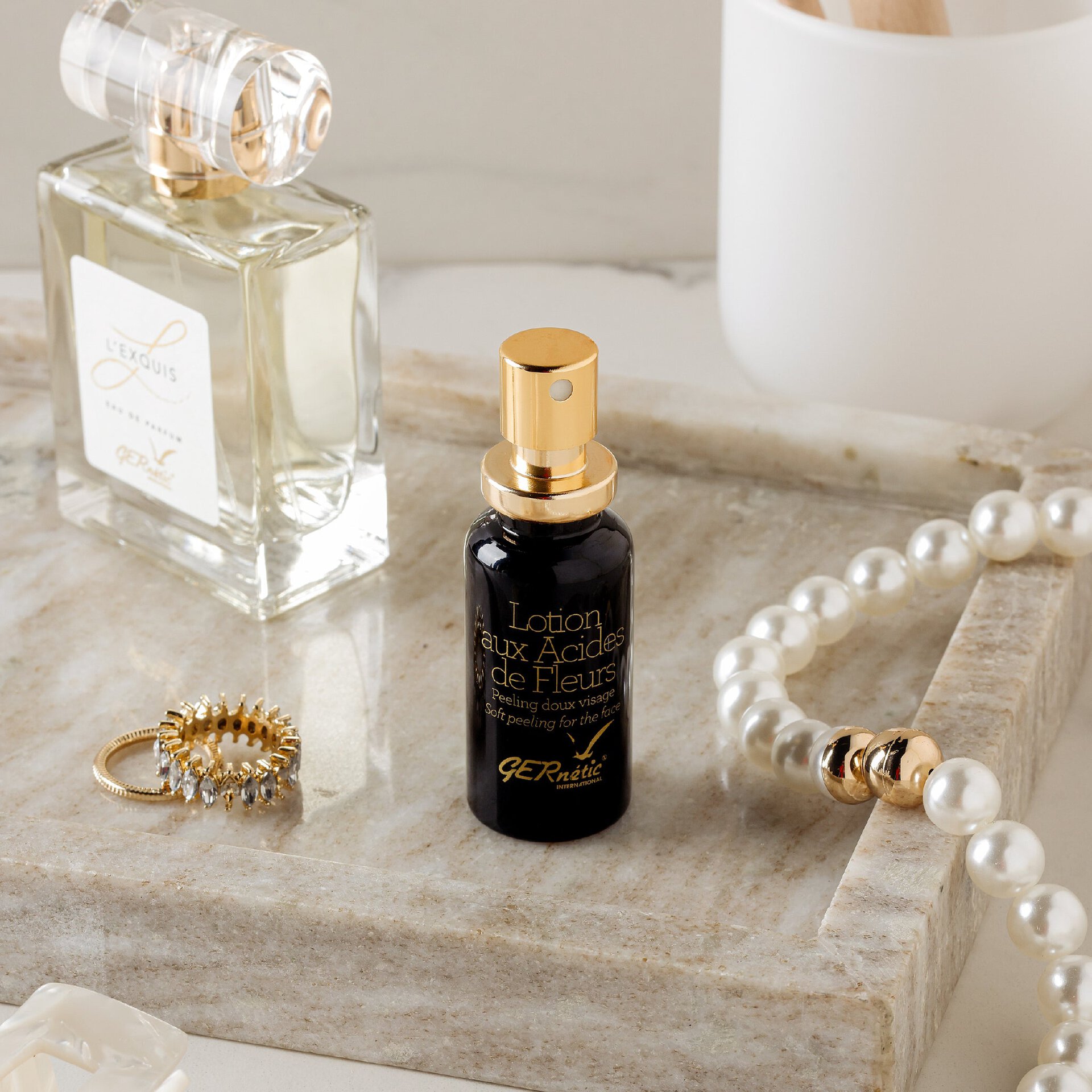 Lotion aux Acides de Fleurs של GERnétic - בקבוק התכשיר על מגש אבן לצד תכשיטים ובקבוק זכוכית