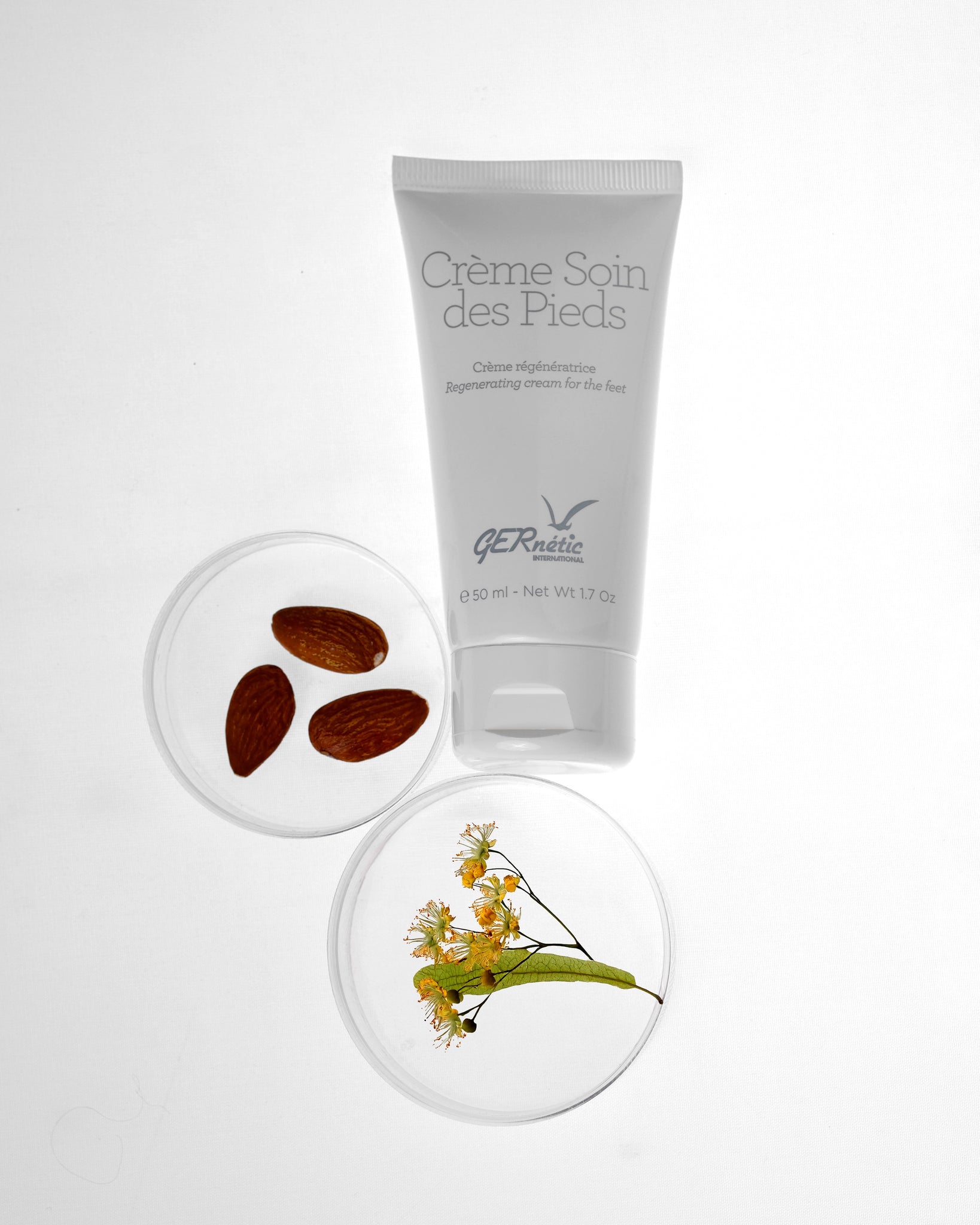 Crème Soin des Pieds של GERnétic – שפופרת קרם לכפות הרגליים לצד שקדים וענף פורח בכלי זכוכית
