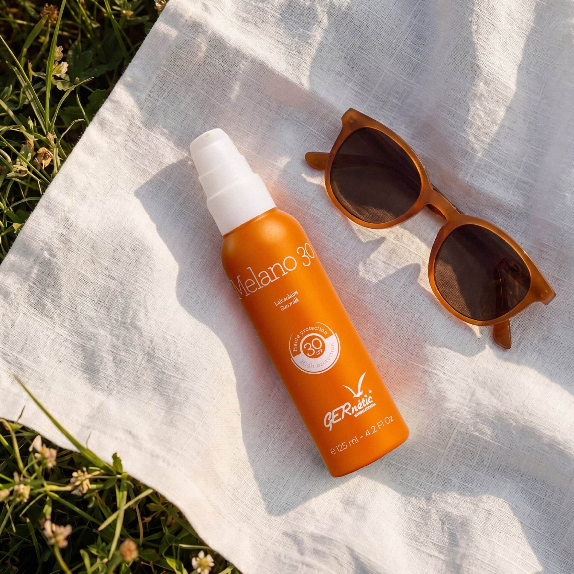 Melano 30 - תחליב הגנה לפנים ולגוף SPF 30; בקבוק מלאנו 30 מונח על בד בהיר לצד משקפי שמש