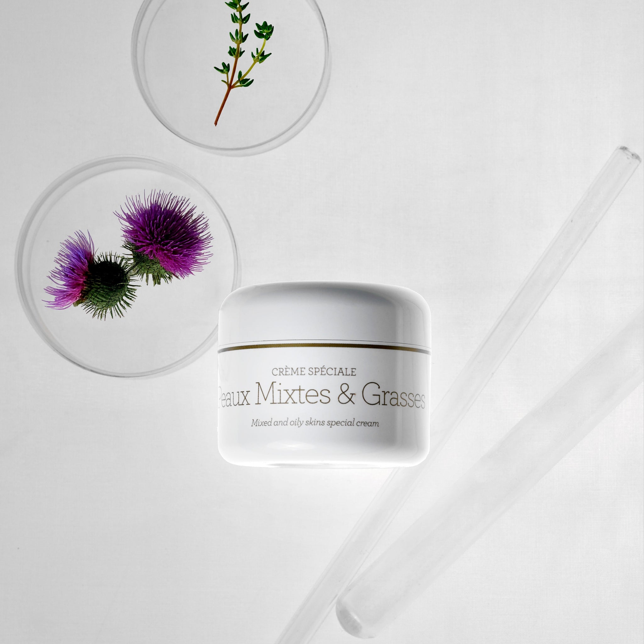 Peaux Mixtes & Grasses של GERnétic - צנצנת הקרם לצד צמחים וכלי זכוכית על רקע לבן