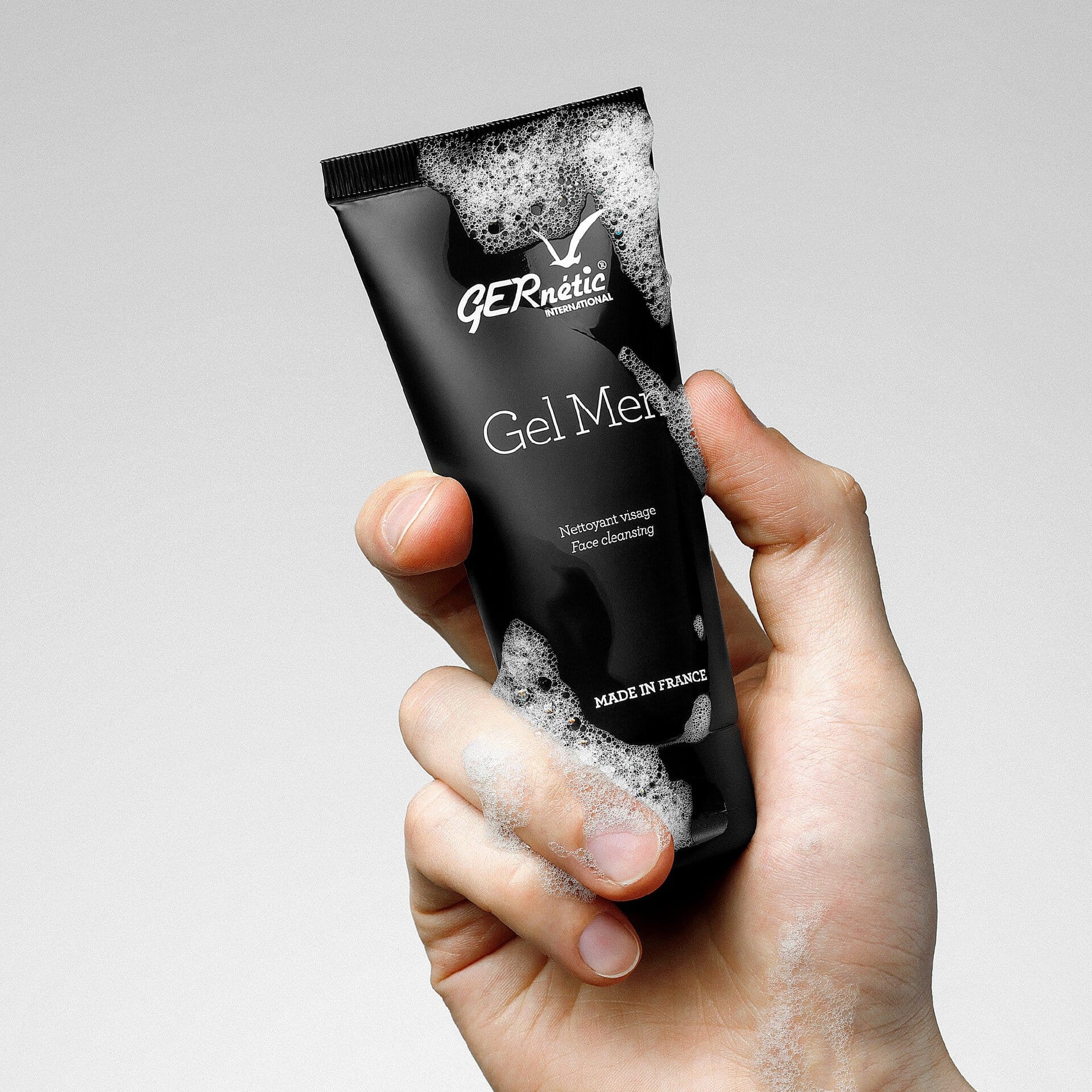 Gel Men של GERnétic - יד מחזיקה שפופרת שחורה של ג׳ל הניקוי, עם קצף על היד ועל האריזה